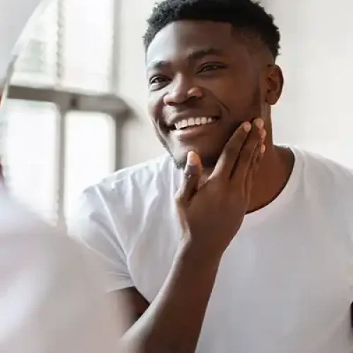 man looking in mirror at his skin and smiling