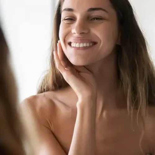 smiling woman looking at her skin in the mirror facials